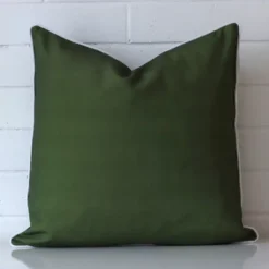White wall with an olive green outdoor cushion laying against it. It has a distinctive waterproof fabric and has a square shape.