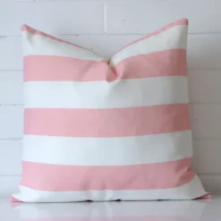 A striped pink outdoor cushion shown front on against a white wall.