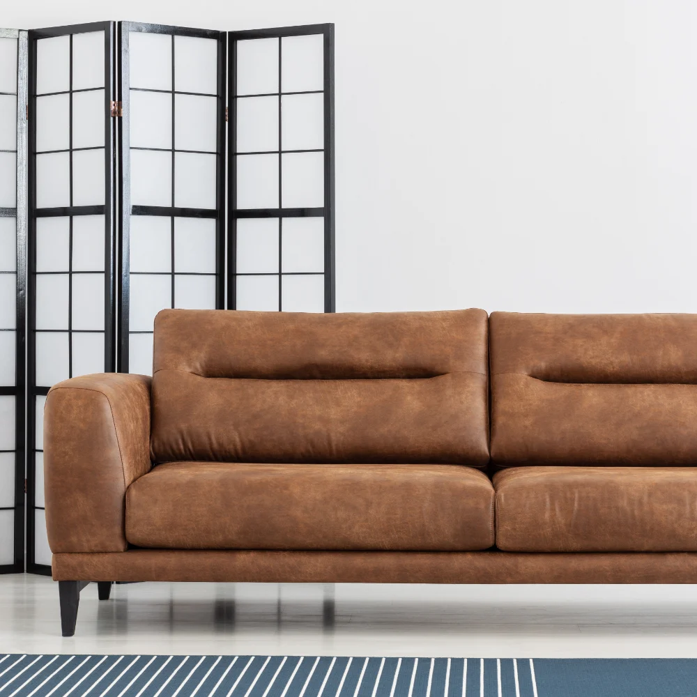 A brown sofa is shown against a light coloured wall and a dark room divider.