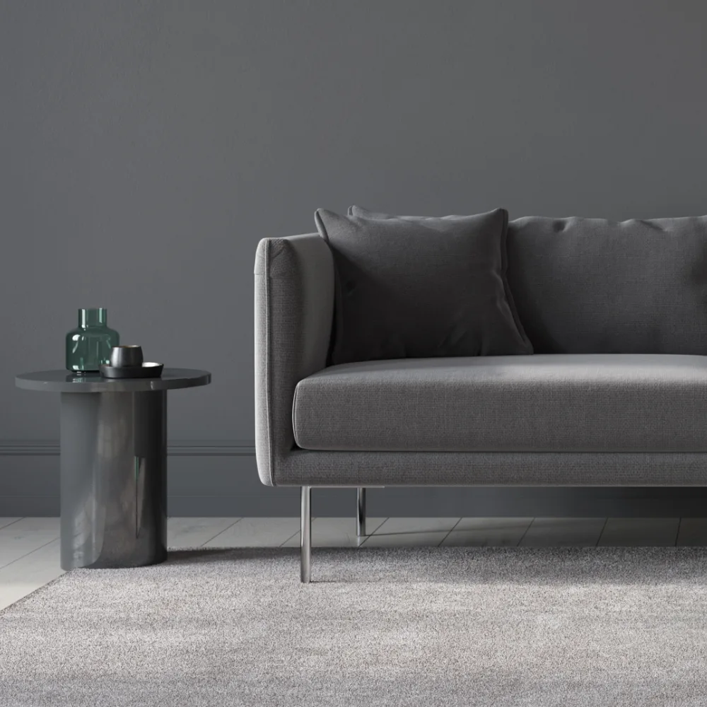 A dark grey sofa is styled in a dark room with a charcoal coloured wall and side table.