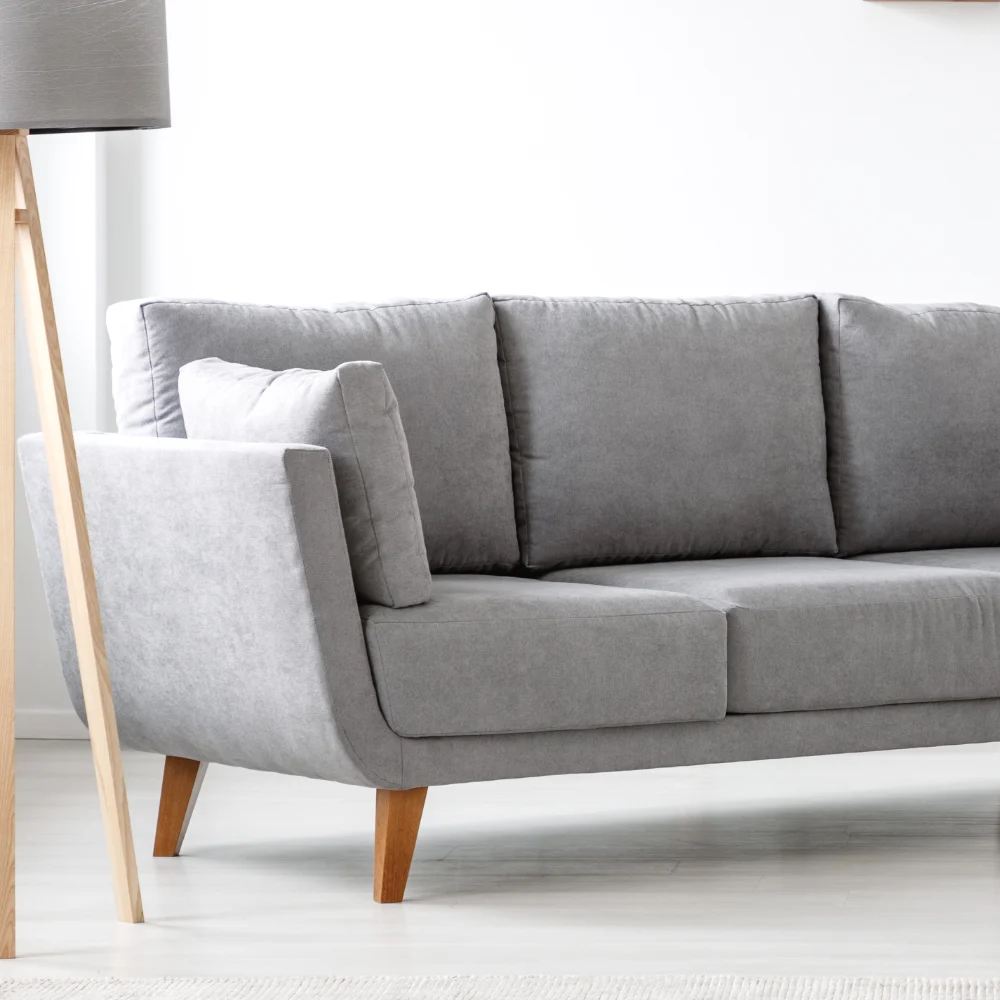 A grey sofa stands in a light coloured room with an elegant wooden lamp standing next to it.