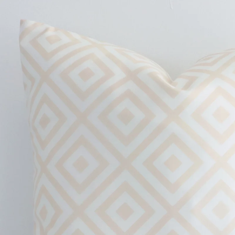 The corner of this beige outdoor cushion is shown close up. The finer detail of its square design and geometric decorative finish can be seen.