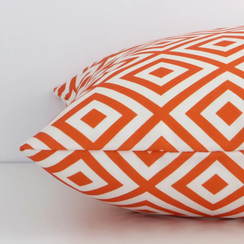 The edge of this outdoor square cushion in orange is shown. The shot shows the geometric design and the front and rear panels.