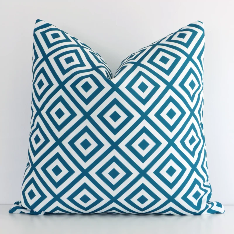 byron-geometric-waterproof-teal-outdoor-cushion-cover---sc723-45 Teal geometric cushion cover in front of a white wall. It has a square size and is made from an outdoor material.