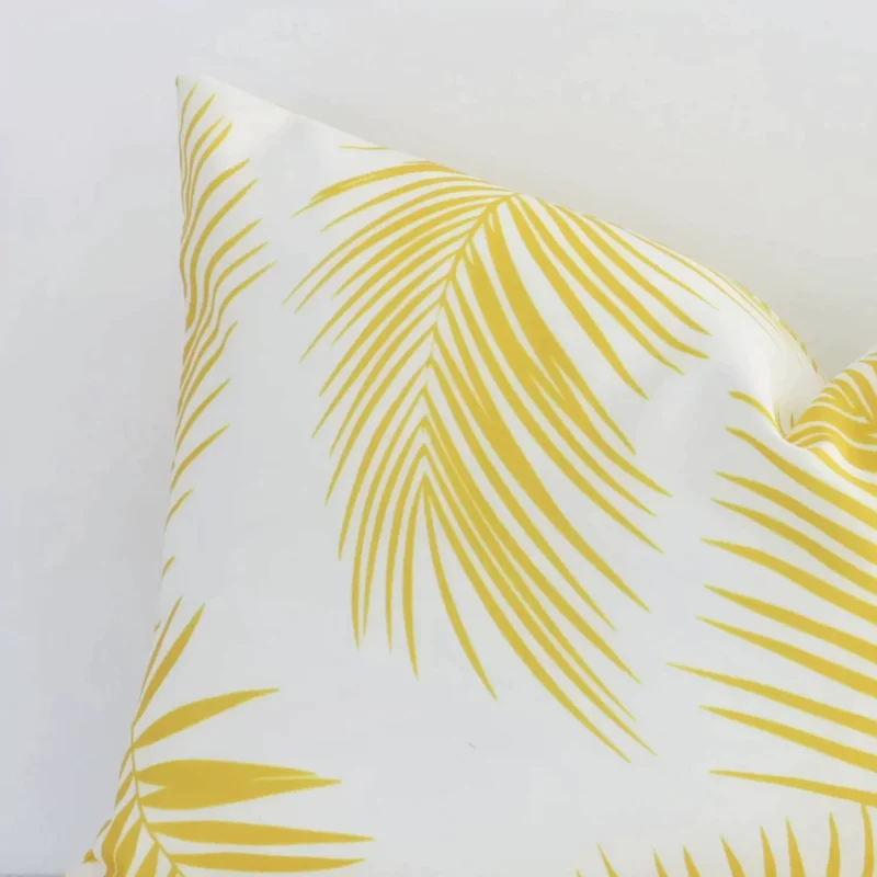 Zoomed photo of the top left corner of this yellow palm printed rectangle cushion cover. The image clearly shows the outdoor material.