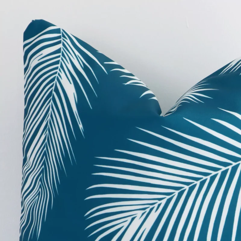 A very close image of the corner of a palm designed outdoor cushion.The finer detail of the square shape and teal colour are visible.
