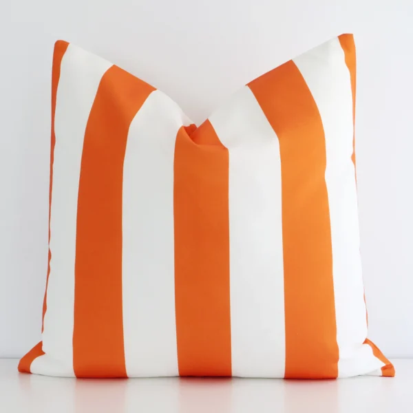 Orange striped cushion leans elegantly against a white wall. It has been crafted from a high quality outdoor material and has a large size.