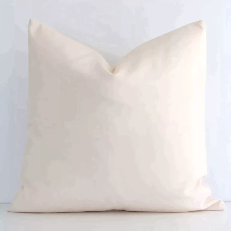 Here a beige outdoor cushion is shown styled against a white wall. It has a square design and features a solid-coloured style.
