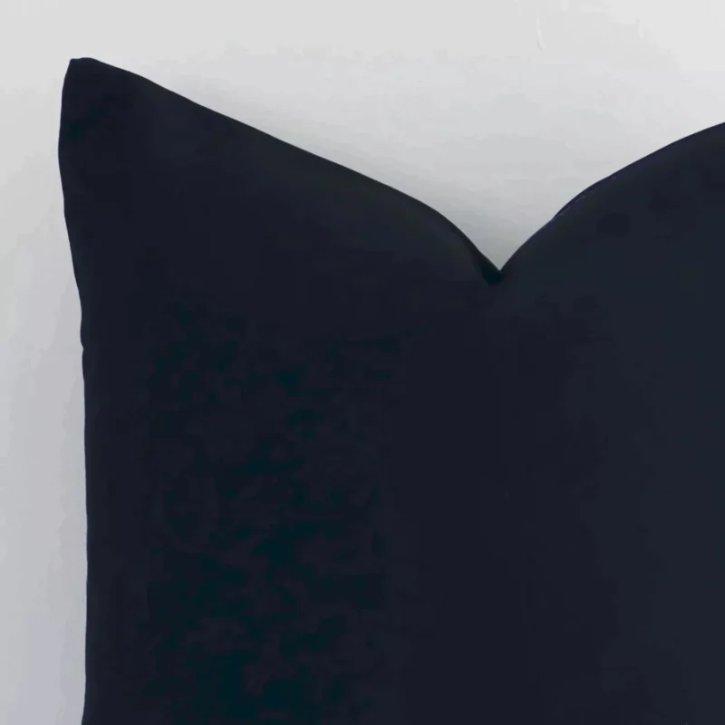 The corner of this black outdoor cushion is shown close up. It has a square shape and a solid-coloured design.