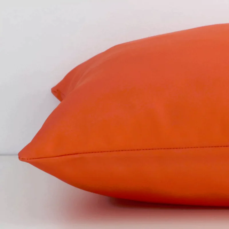 Bold orange cushion laid horizontally. This perspective shows the edge of the outdoor fabric and its square shape.
