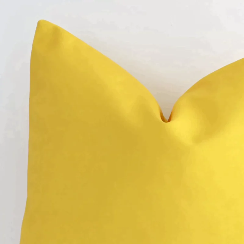 Focused view of solid-coloured square cushion cover. The shot shows details of its outdoor material and yellow colour.