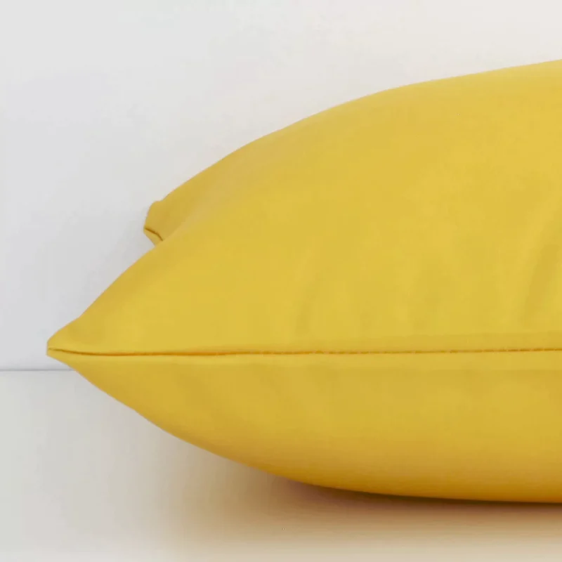 Side perspective showing seam of square solid-coloured yellow cushion cover that has a an outdoor fabric.