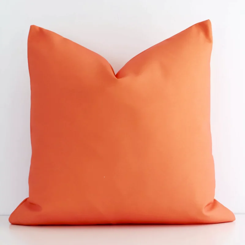 caravan-coral-waterproof-outdoor-cushion-cover---sc579-45 An attractive solid coloured outdoor cushion in front of a white brick wall. It has a square shape and is coral in colour.