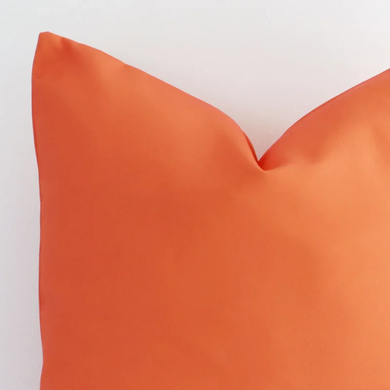 Macro shot showing the top left side of this square outdoor cushion. The coral hue and solid-coloured design are magnified.