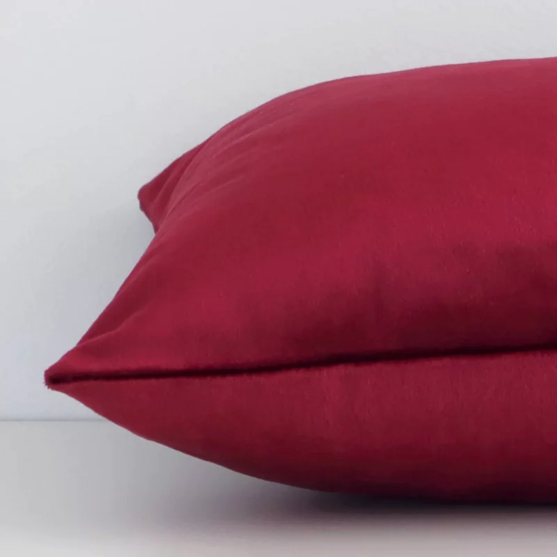 Side angle of burgundy solid-coloured cushion cover that has velvet fabric and a rectangle size.
