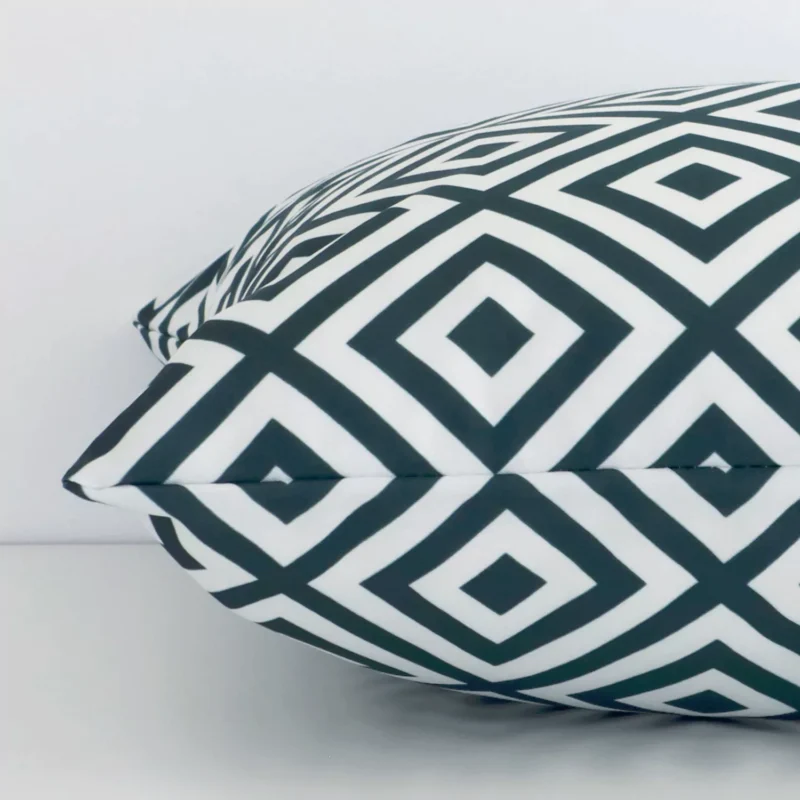 A geometric green cushion cover is laid flat. This angle shows the side of the outdoor fabric and its square shape.