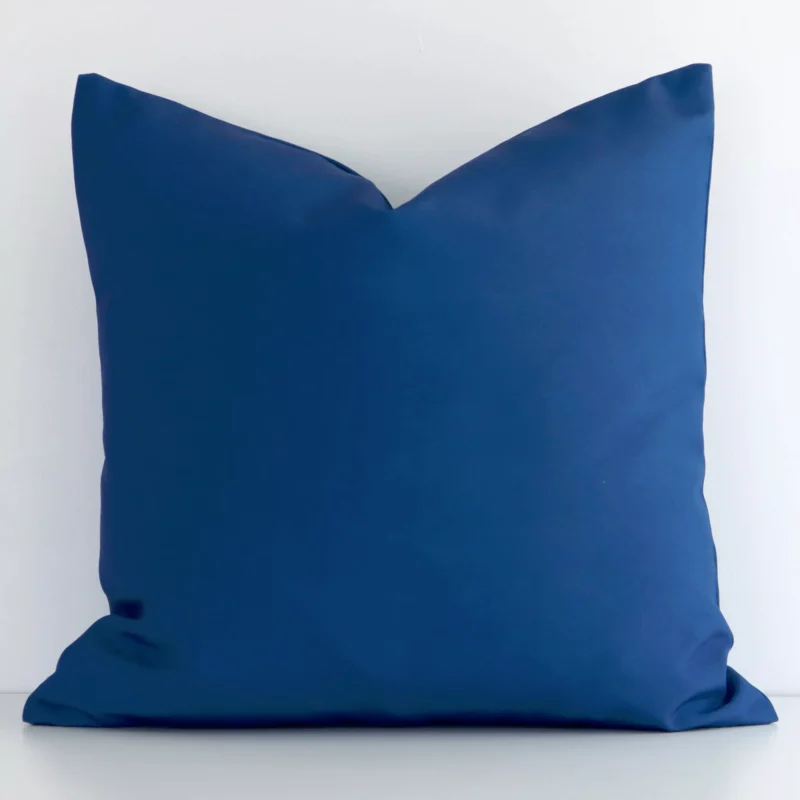 byron-waterproof-blue-outdoor-cushion-cover---sc954-45 White wall with a bold blue cushion laying against it. It has a distinctive outdoor fabric and has a square shape.