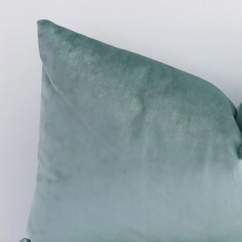 The corner of this mint green velvet cushion is shown close up. The finer detail of its rectangle design and solid colour finish can be seen.