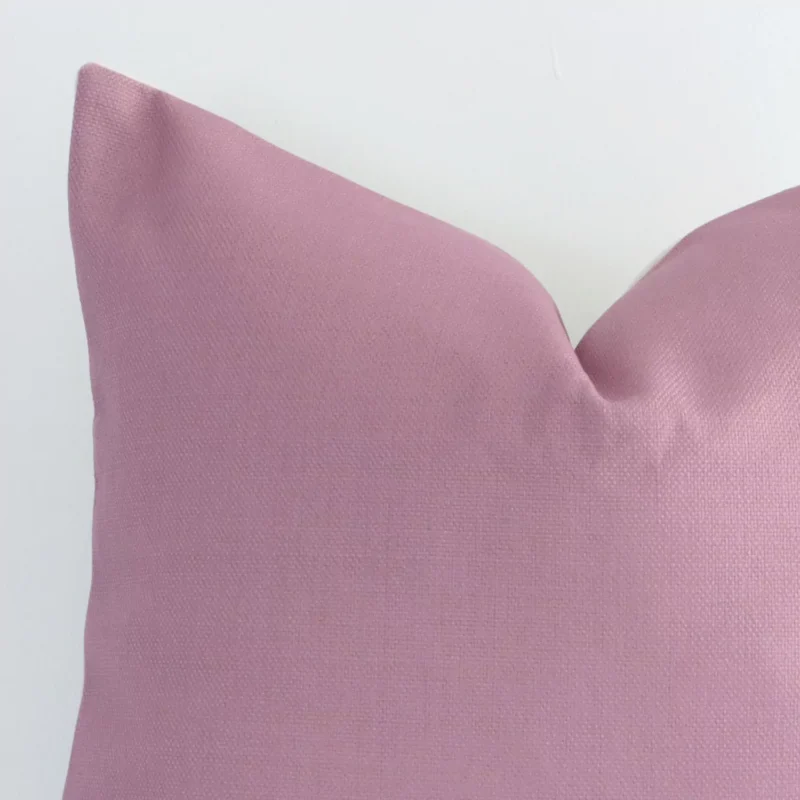 A blush linen cushion cover’s corner is shown in more detail. It is possible to see the square design and solid-coloured finish in much more detail.