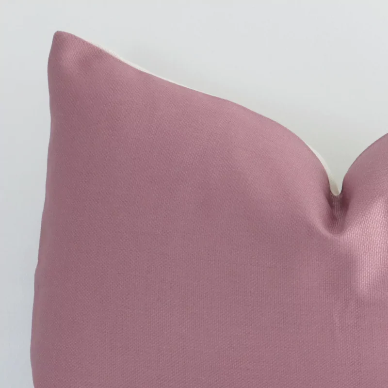 A linen rectangle cushion’s corner has been enlarged in this shot. The detail of the solid-colour blush colour is visible.
