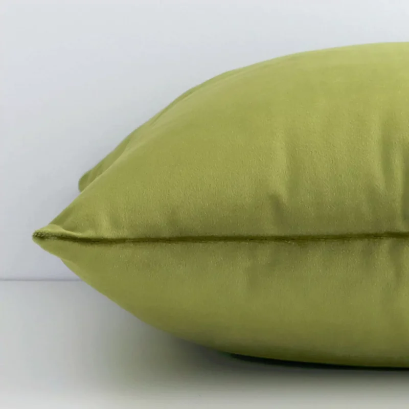 Square olive green cushion laid flat. This view shows the velvet fabric from side on.