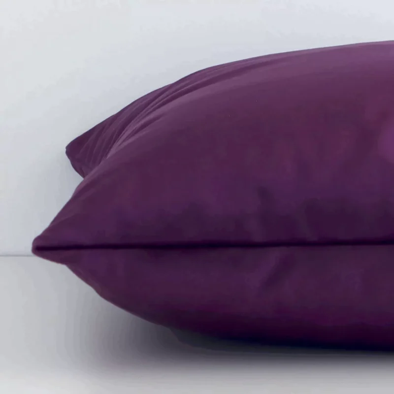 Side edge of solid-coloured square cushion. The velvet material and plum purple colour can be seen from this lateral viewpoint.