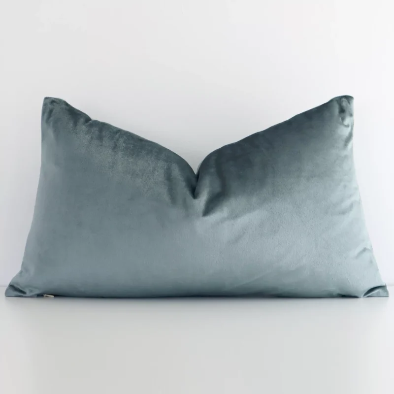 sage-green-velvet-linen-rectangular-cushion-cover---rectangle---sc784-30 White wall with a solid-coloured sage green cushion laying against it. It has a distinctive velvet fabric and has a rectangle shape.