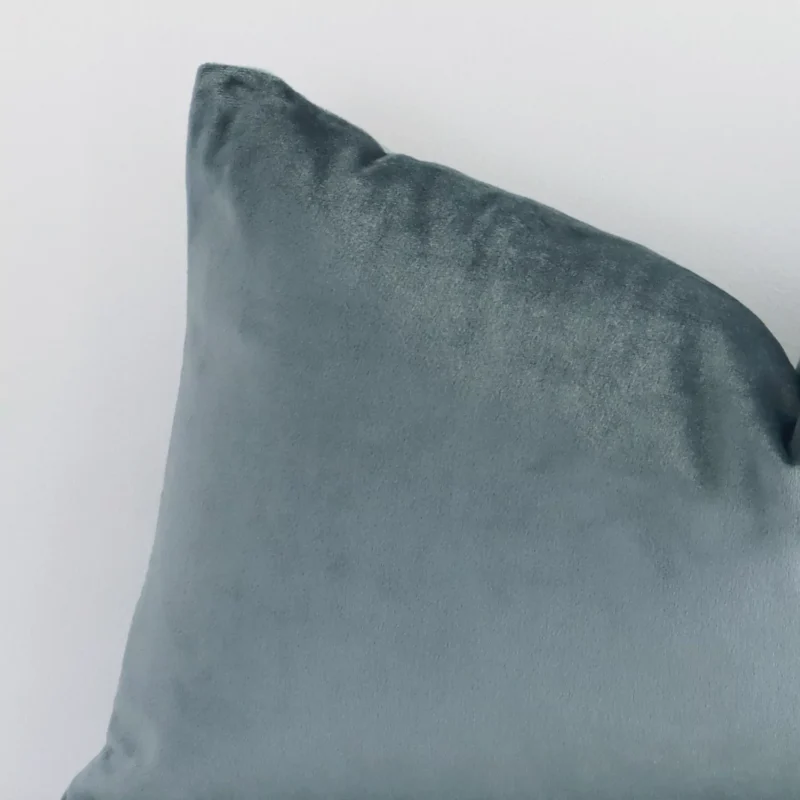 Close up view showing a corner of this solid-coloured velvet cushion in a square size and with sage green colouring.