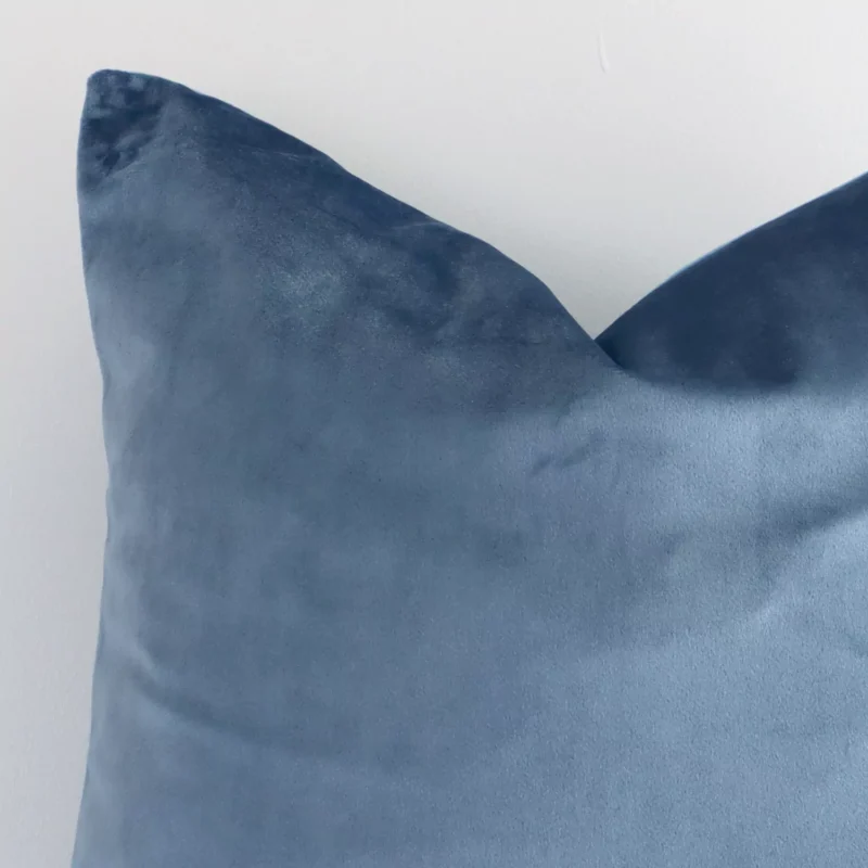 A stone blue square cushion cover’s corner is shown in more detail. It is possible to see the velvet material in much more detail.