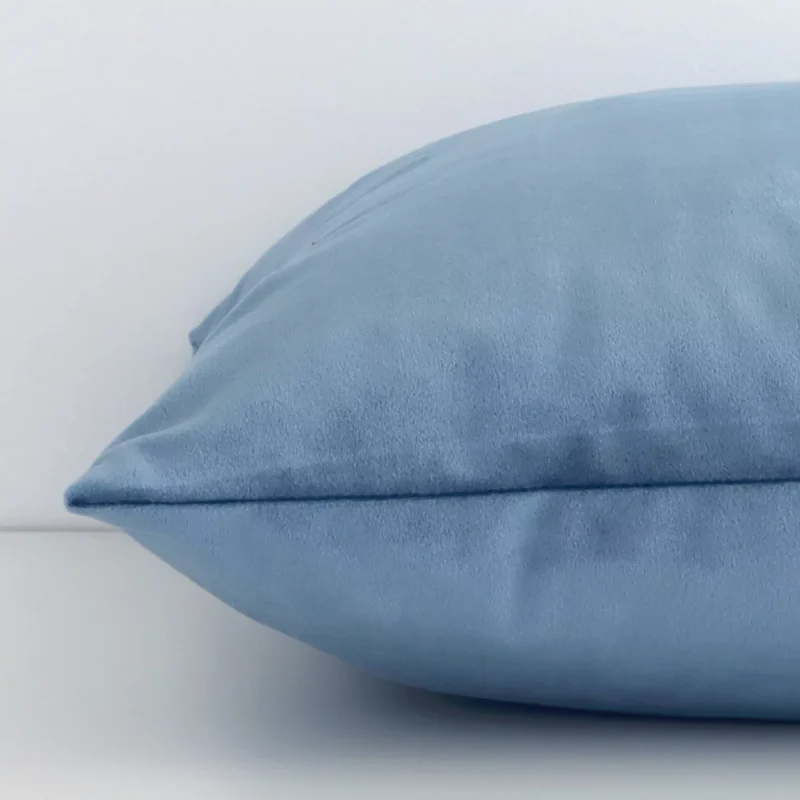 A stone blue solid-coloured cushion positioned on its back panel. The shot shows a lateral view of the velvet fabric and its square shape.