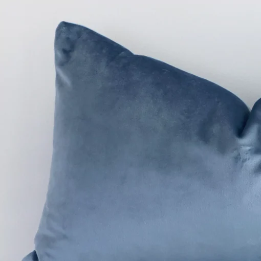 A velvet rectangle cushion’s corner has been enlarged in this shot. The detail of the solid colour design and stone blue colour are visible.