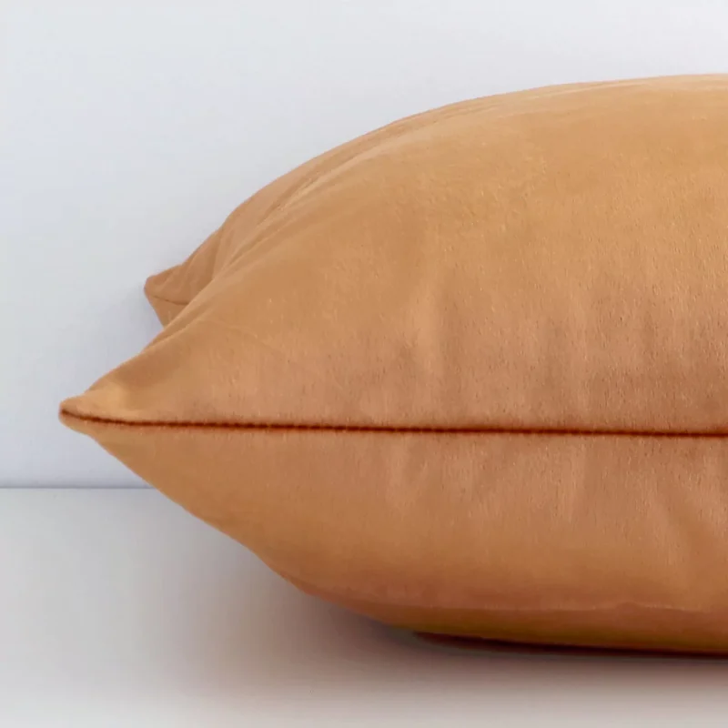 A solid terracotta colour cushion cover is laid flat. This angle shows the side of the velvet fabric and its square shape.