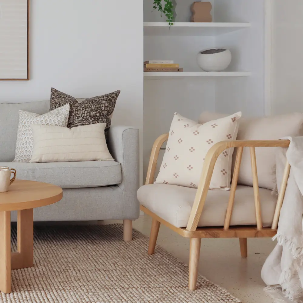 Indoor cushions arranged in a living room on a light wooden armchair and sofa with a natural rug on the floor.
