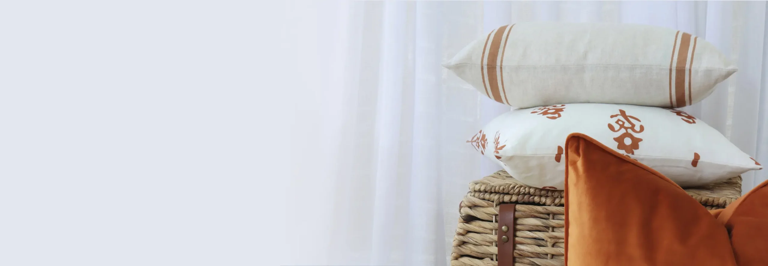 Classic cushions arranged on top of and in front of a cane basket with a curtain backdrop.