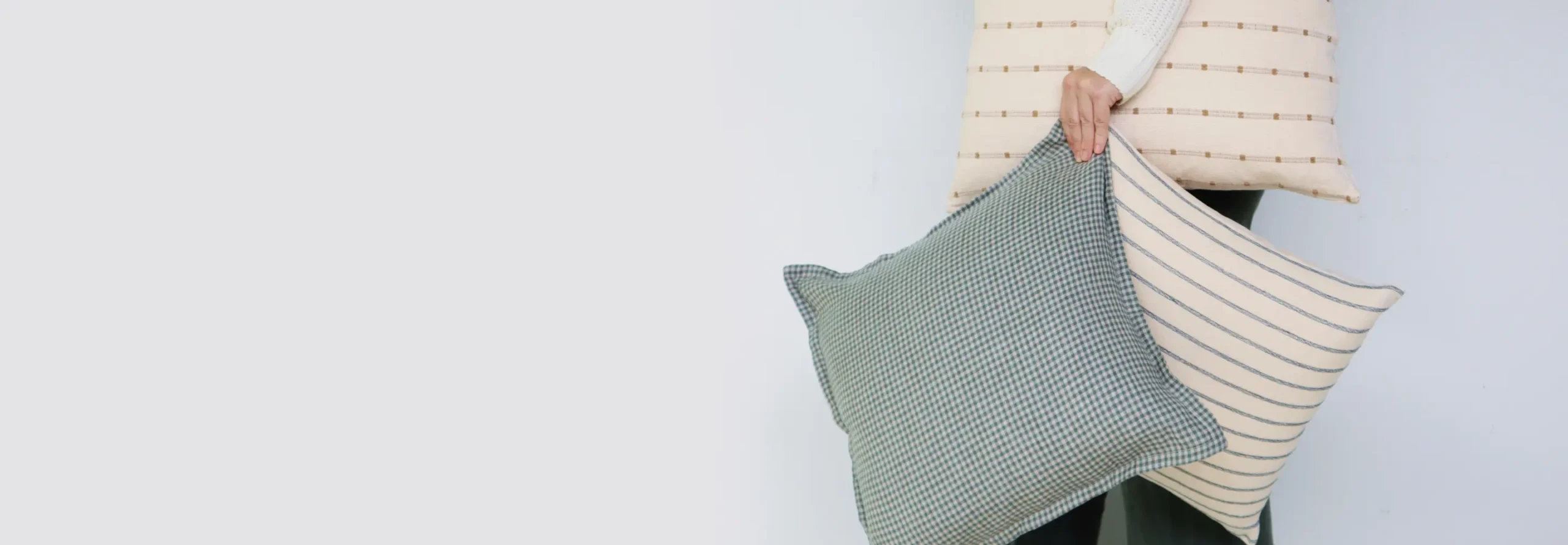 Cushions and cushion covers are being carried by a person in front of a light background.