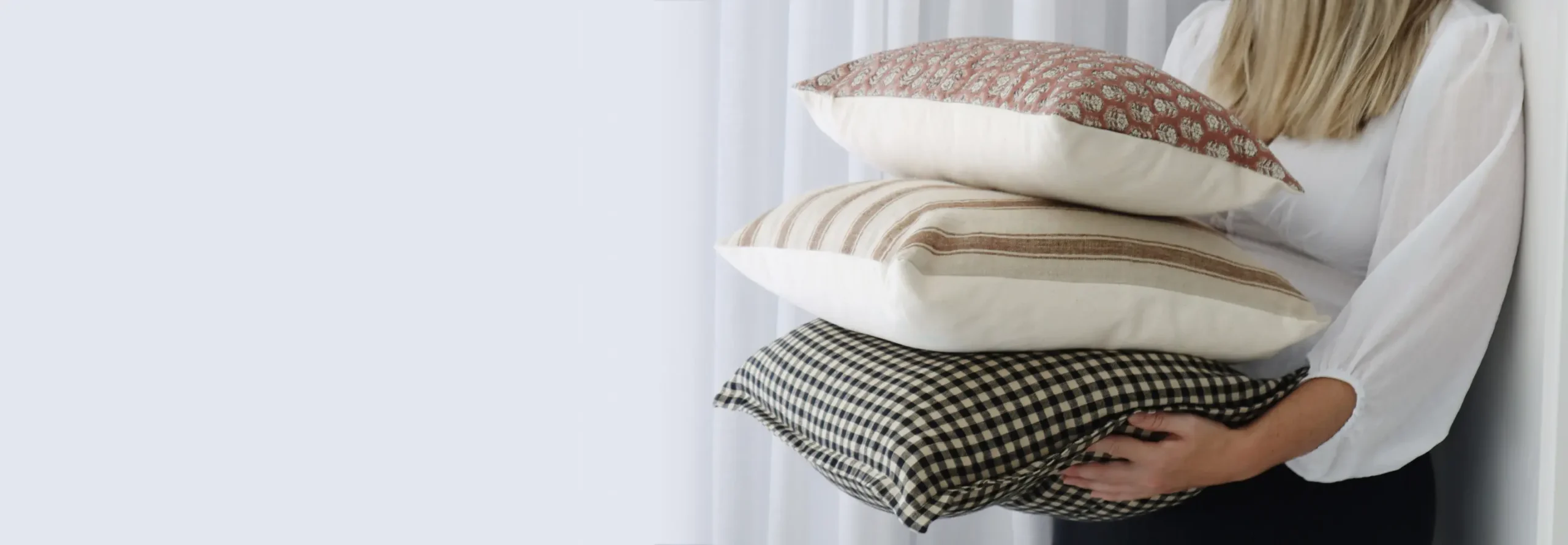 Designer cushions in various designs and sizes being held by a lady in a white shirt.