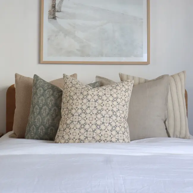 A collection of five large cushions on top of a bed with a picture frame above them.