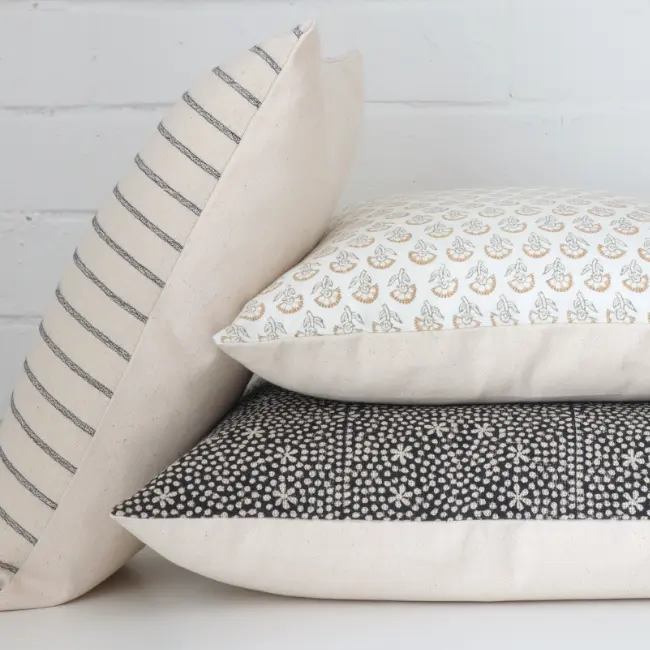 Three designer cushions lay neatly arranged against a white brick wall.