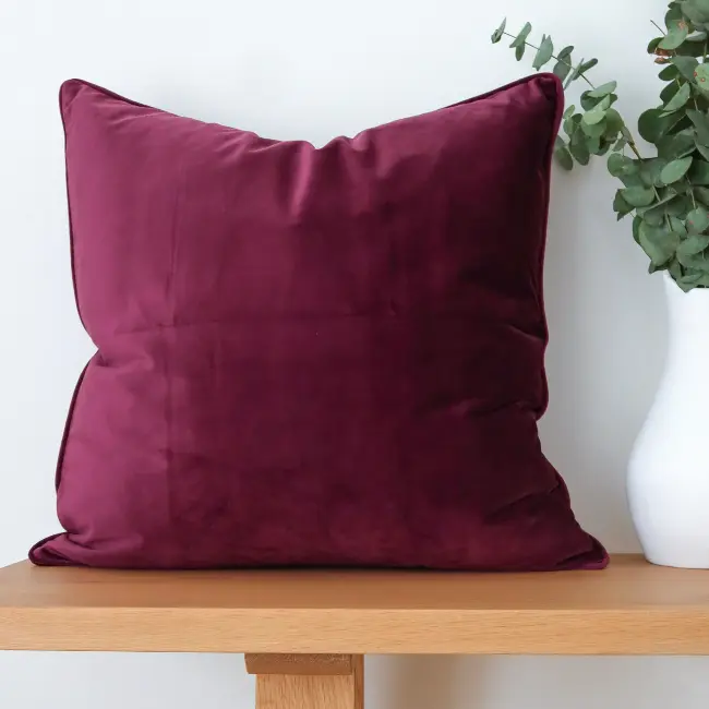 A bench made of wood has a velvet cushion and vase styled on it.