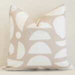 Sand geometric cushion cover in front of a white wall. It has a square shape and is made from an outdoor material.