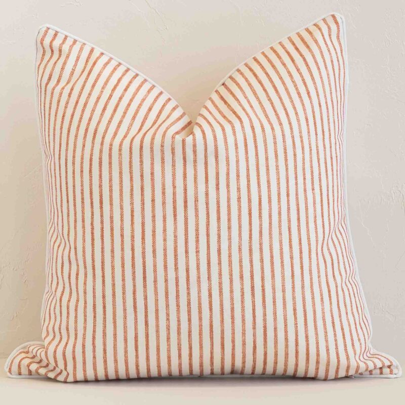 Pacific Rust Waterproof Pinstriped Outdoor Cushion Cover - SC1060-45 Bold square rust cushion positioned in front of white brickwork. Its striped style pops on the outdoor fabric.