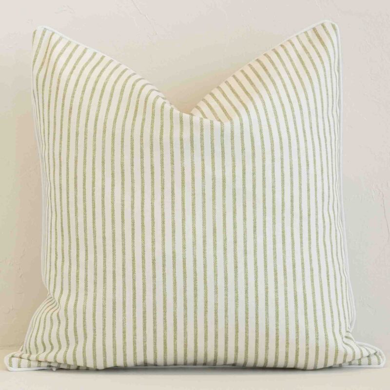 An attractive striped outdoor cushion in front of a white brick wall. It has a square shape and is sage in colour.