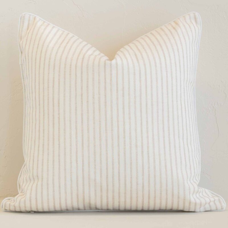 White wall with a stripe sand cushion laying against it. It has a distinctive outdoor fabric and has a square shape.