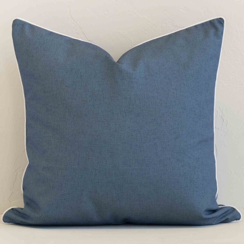 Outdoor large cushion with a solid- coloured design in an upright position against a white brick wall.