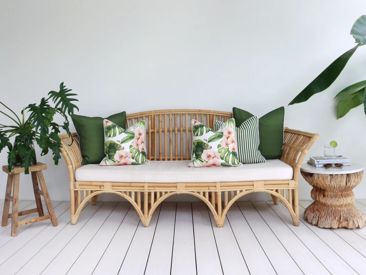 A collection of green outdoor cushions featuring some tropical prints sit arranged on an outdoor sofa in front of a white wall.