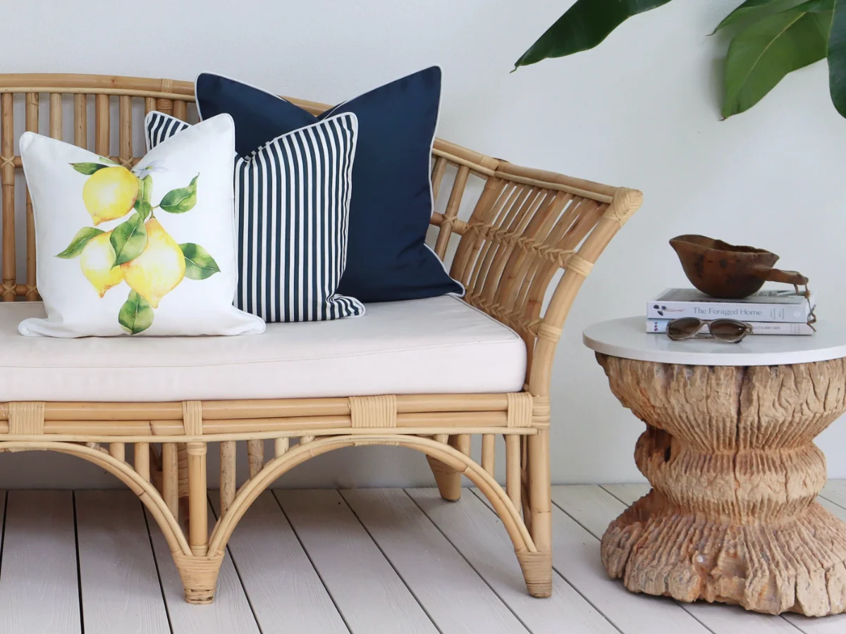 A lemon print outdoor cushion is positioned in front of some navy coloured designs on a seat on an outdoor deck.
