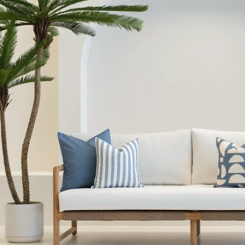 A set of 3 outdoor cushions in a pacific blue colour are displayed on on white sofa.