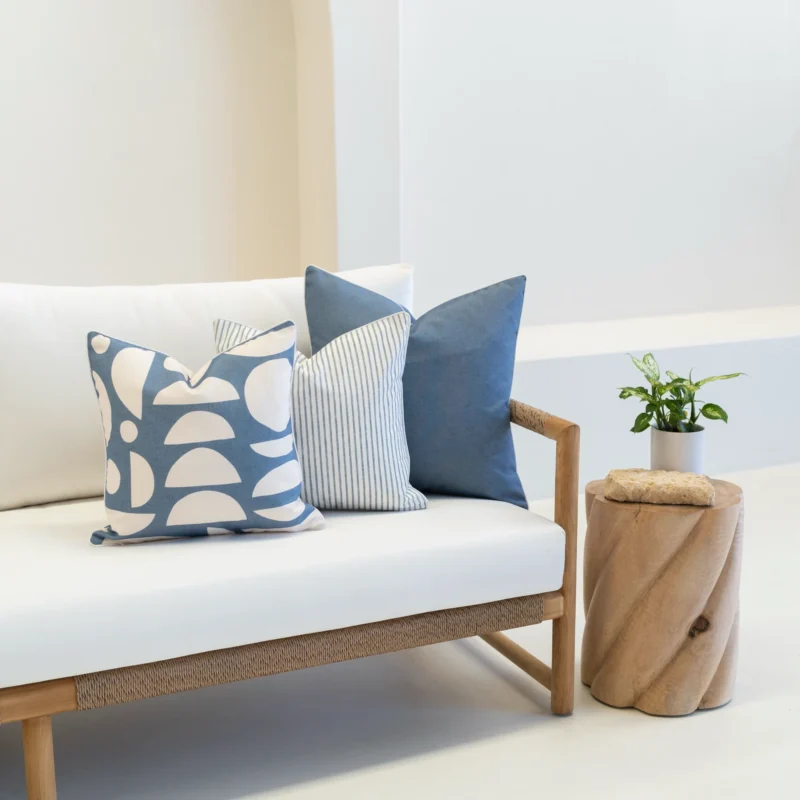 Corner of a white sofa with a set of 3 pacific blue oudoor cushions on its corner.