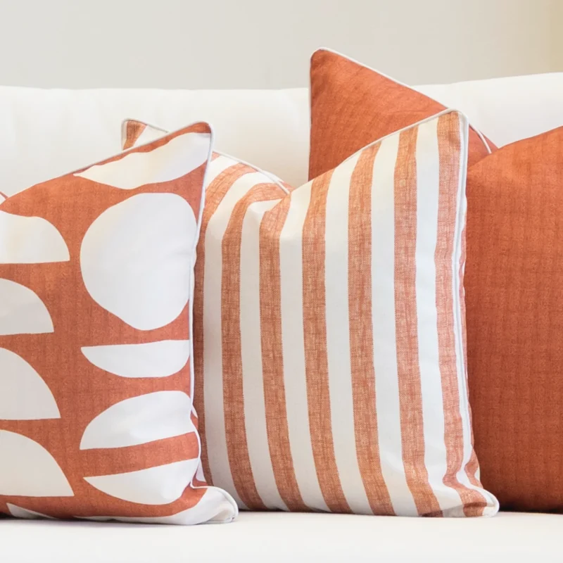 A set of 3 pacific rust outdoor couch cushions sitting on a white couch.