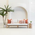 A white outdoor living space featuring a wooden sofa styled with a set of five Pacific Rust outdoor cushions.